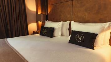 A neatly made bed with white linens and black pillows with a monogram, a bedside table with a lamp, and a wooden headboard.