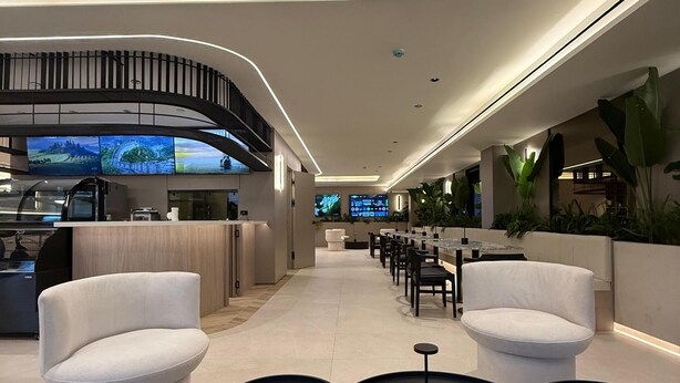 Een moderne lounge met zitplaatsen, tafels en een groot scherm dat een prachtig uitzicht toont.