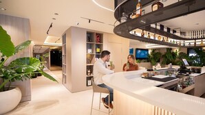 Een moderne bar met een gebogen toonbank, planken met flessen en een zithoek met een barstoel.