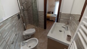 Een moderne badkamer met een douchecabine van glas, een toilet, een bidet en een wastafel met spiegel.
