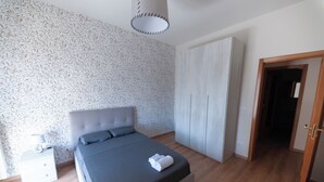 Een slaapkamer met een bed, een kledingkast, een nachtkastje en een deur naar een andere kamer.