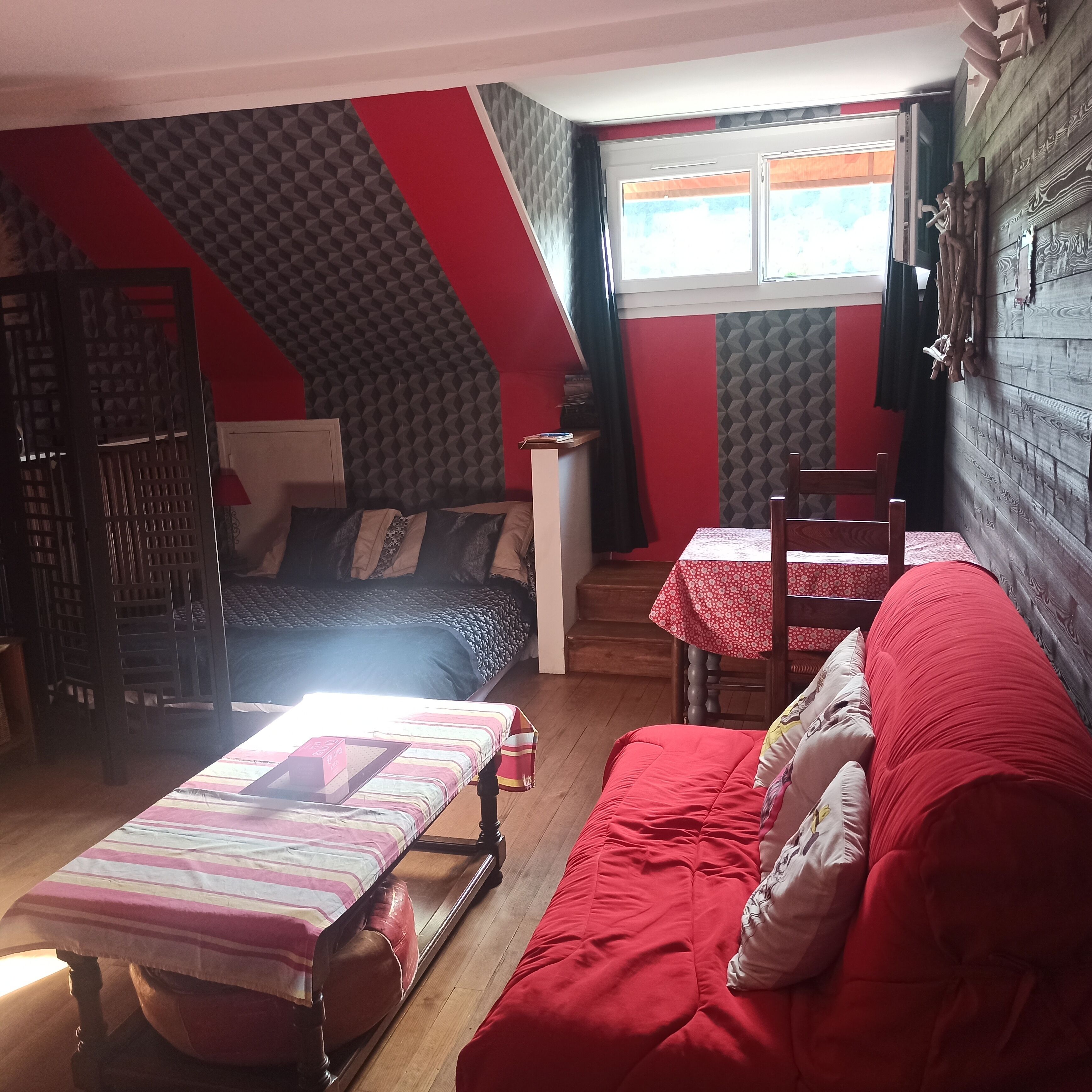 A room with a bed, a red sofa, a dining table with chairs, and a window with curtains.