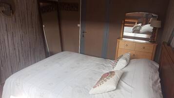Een slaapkamer met een bed, een houten nachtkastje, een spiegel en een deur.