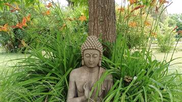 En statue af en siddende figur omgivet af frodigt grønt og orange blomster.