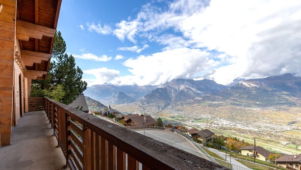Un balcón de madera con vistas a un valle y montañas.