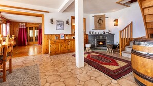 Amplia sala de estar con piso de madera, chimenea, escalera y comedor con mobiliario de madera.