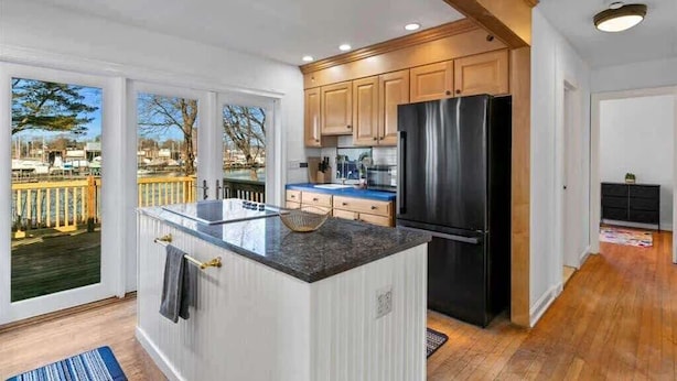 A modern kitchen with a large island, wooden cabinets, and a black refrigerator.