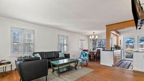 A spacious living room with a black leather sofa, a green coffee table, and a dining area with a blue floral chair.