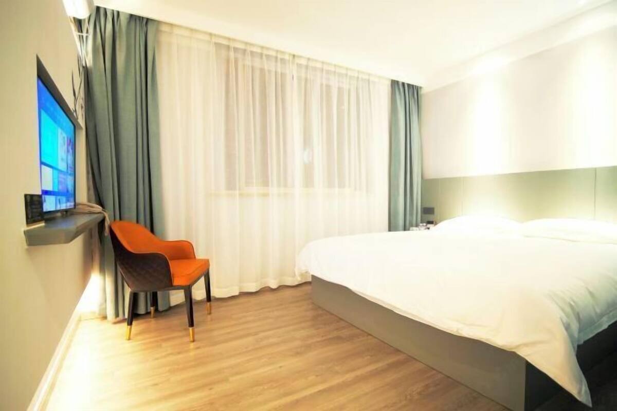 Une chambre d’hôtel avec un lit, un bureau équipé d’un ordinateur, une chaise et une grande fenêtre avec des rideaux.