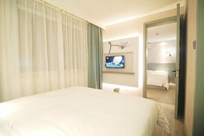 Ein Hotelzimmer mit einem Bett, einem Fernseher, einem Spiegel und einer Tür zu einem weiteren Raum.