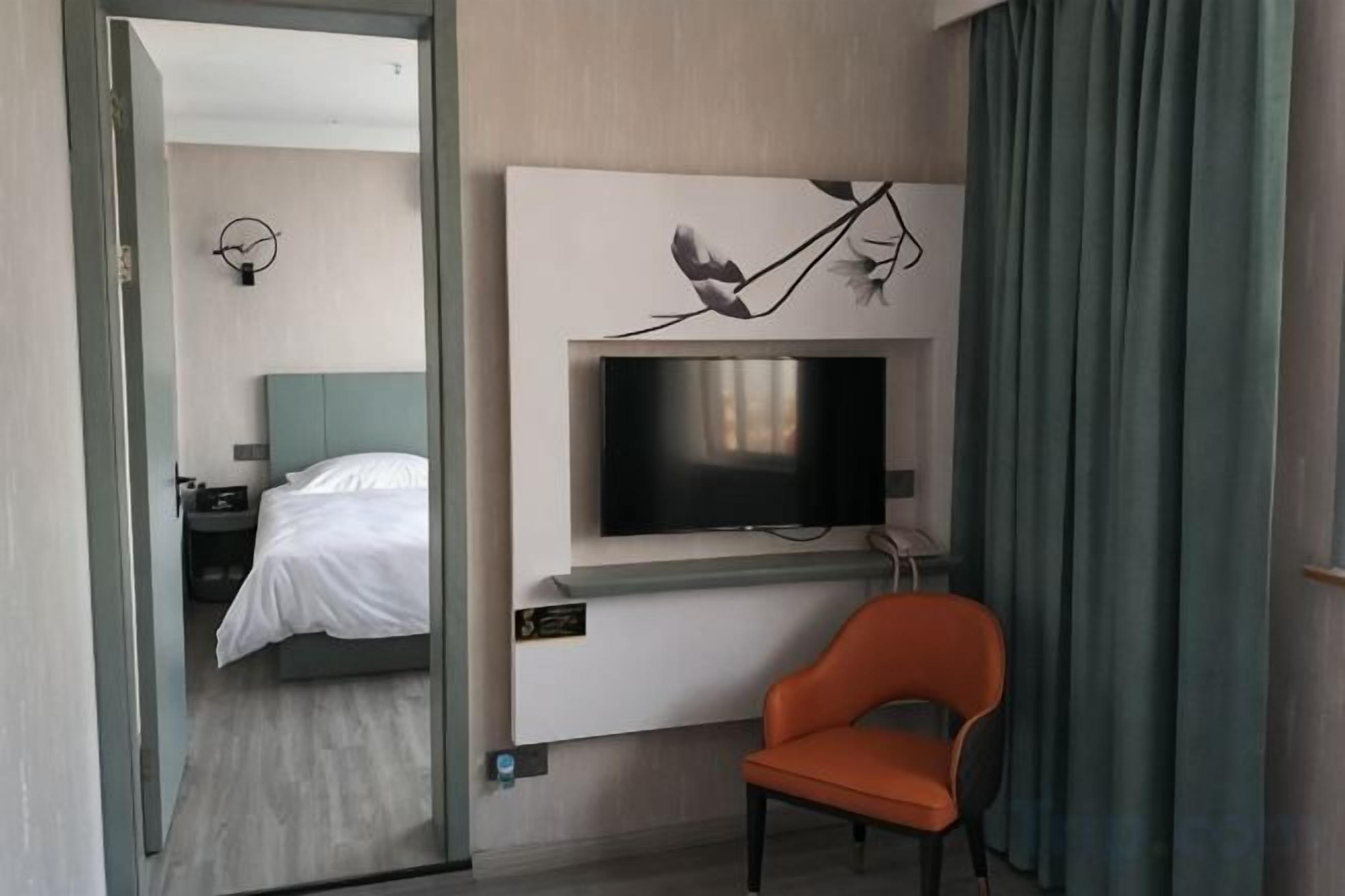 A hotel room with a bed, a TV mounted on the wall, and a chair.