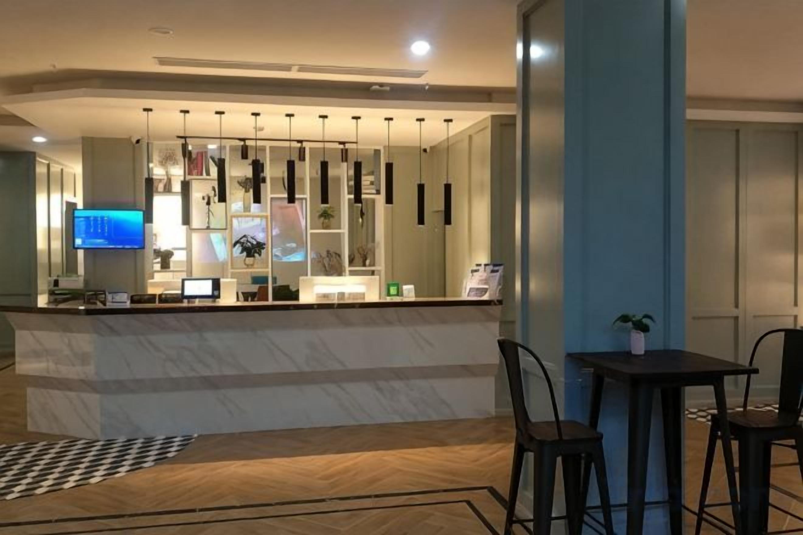 A hotel reception area with a marble counter, modern pendant lighting, a television, and a small table with chairs.