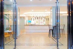 Un vestíbulo de hotel con mostrador de recepción, zona de estar y puertas de vidrio que dan a las habitaciones.