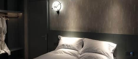 A bedroom with a bed, a bedside table, a clock, and a wardrobe.