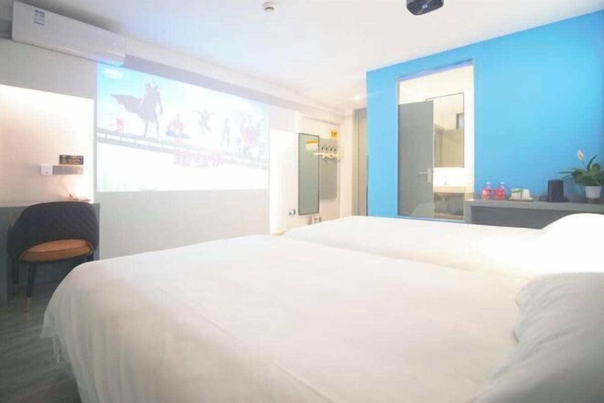 Une chambre d’hôtel équipée d’un lit, d’un bureau, d’une chaise, d’un miroir et d’un écran de projection.