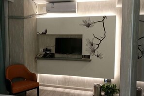 A modern living room with a flat-screen TV, a sofa, a decorative wall with branches and flowers, and a small shelf with a plant. - Jinhuangchao Light extravagance Hotel (Shanghai)