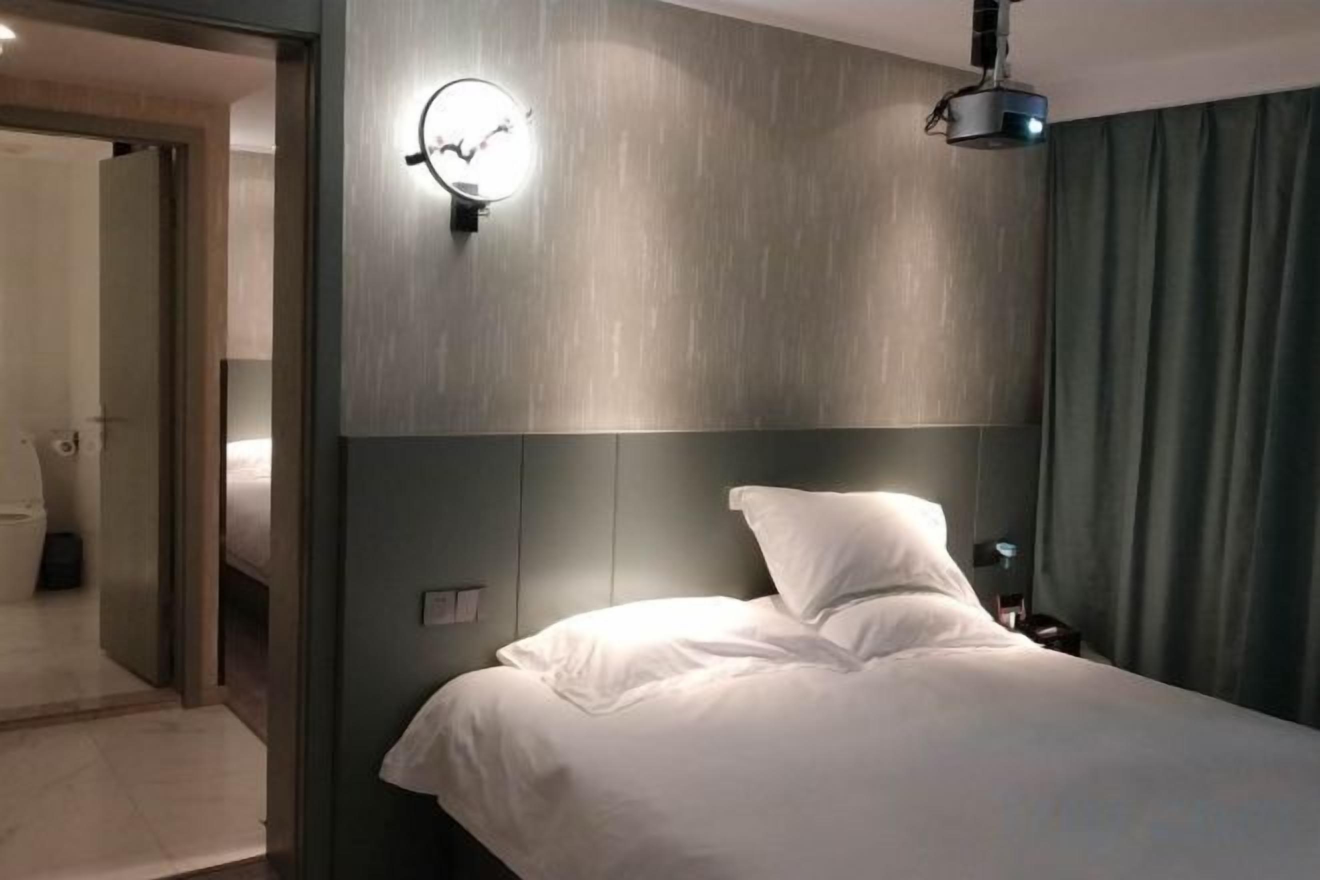 Ein Hotelzimmer mit Bett, Wandleuchte und Deckenprojektor.