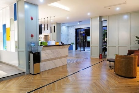 A hotel lobby with a reception desk, a water dispenser, a small refrigerator, a seating area with a sofa, and a view of the dining area.. Jinhuangchao Light extravagance Hotel