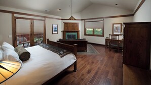 Un dormitorio espacioso con una cama grande, piso de madera, chimenea y vistas al exterior.