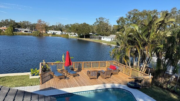A pool with a wooden deck, lounge chairs, and a red umbrella. - Paradise Lake (Clearwater)