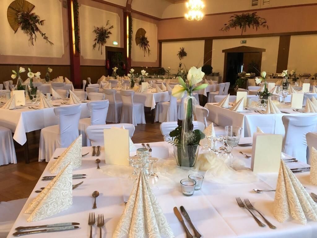 A banquet hall with round tables set for a formal event, featuring white tablecloths, elegant centerpieces, and neatly arranged cutlery.