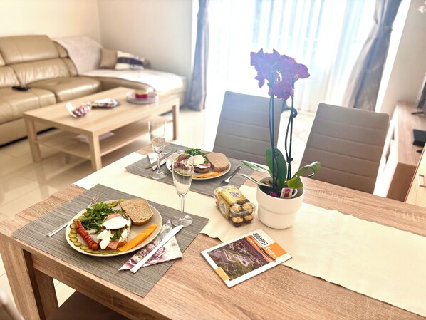 Een eettafel gedekt met een sandwich, een glas water, een bord olijven, een klein bakje noten en een brochure.
