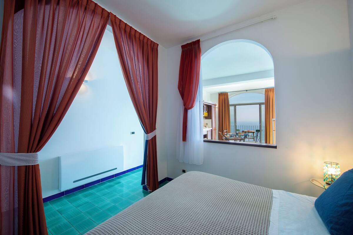 A hotel room with a bed, a window with curtains, a mirror, and a view of the pool area.