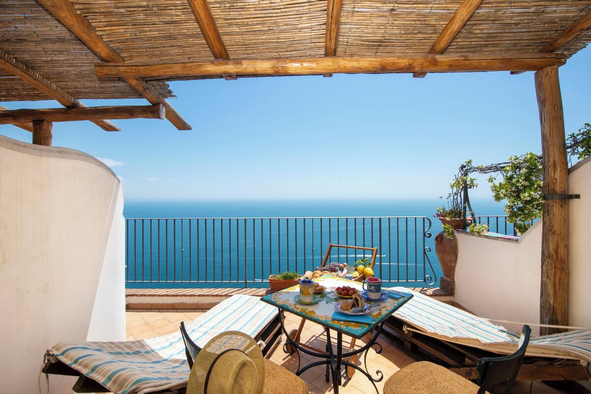 A terrace with a table set for dining, overlooking the sea.