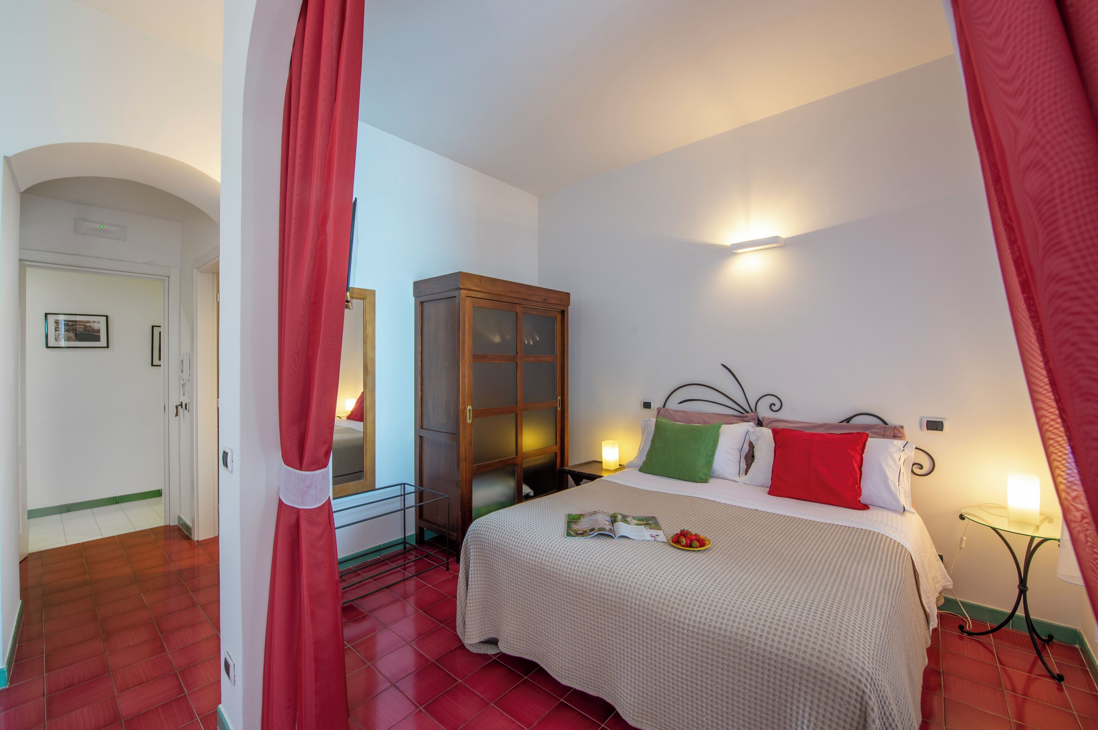 A bedroom with a bed, a wooden cabinet, a bedside table with a lamp, and a red curtain.