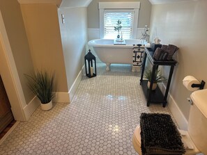 A bathroom with a white bathtub, a black vanity, a hexagonal tiled floor, a potted plant, and a window with blinds. - Thompson House #3-Overlooking City Park. Walk to Campus, Aggieville & Downtown (Manhattan)