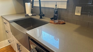 Una cocina moderna con un lavamanos de acero inoxidable, un grifo negro y una tabla de cortar de madera con una botella de TH 1912 en la encimera.