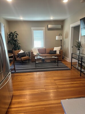 A living room with a brown leather sofa, a glass coffee table, and a striped rug. There is a potted plant, a lamp, and a TV on a stand. - Thompson House #3-Overlooking City Park. Walk to Campus, Aggieville & Downtown (Manhattan)