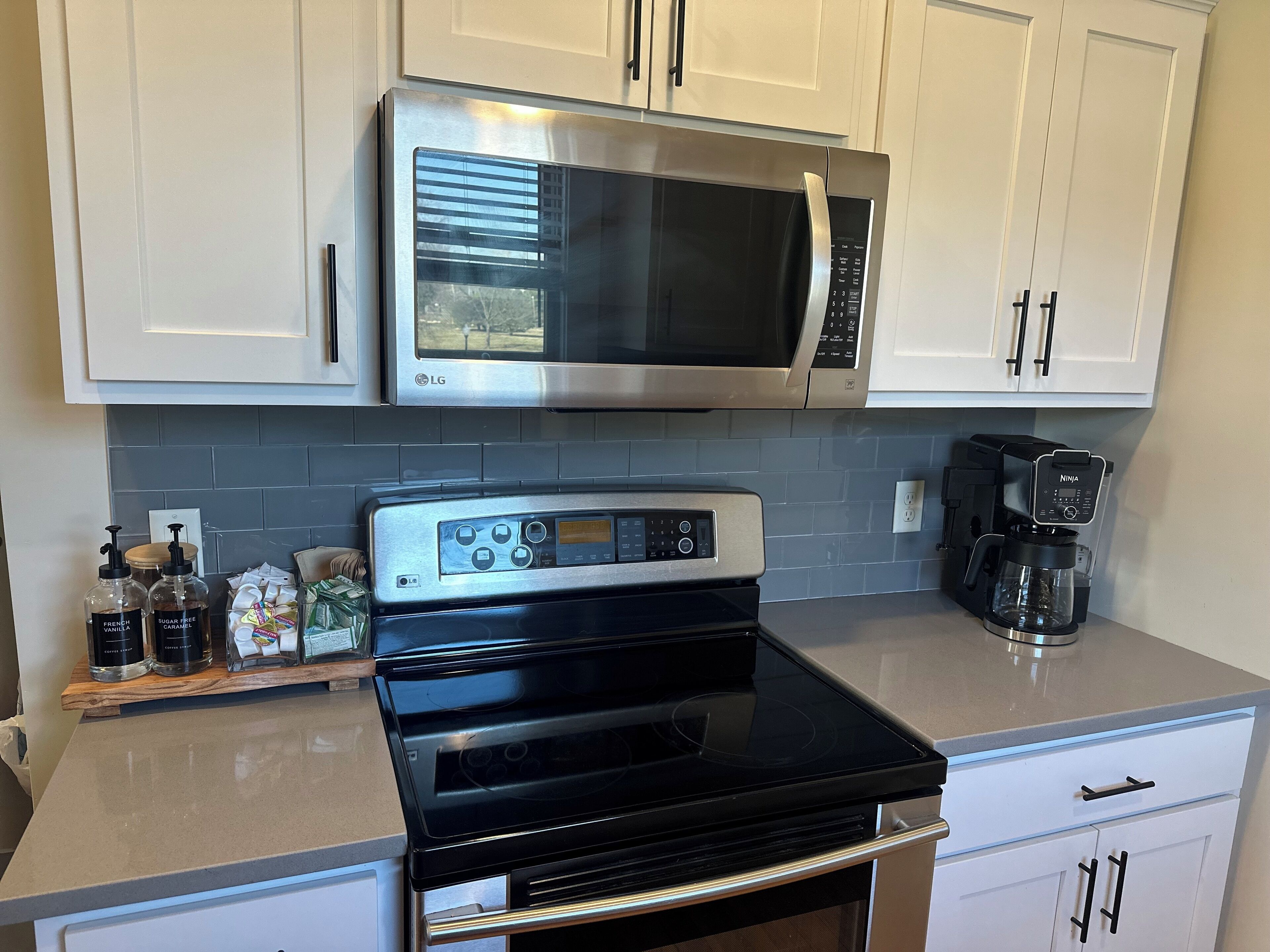 A kitchen with white cabinets, a stainless steel microwave, a black stove, and a coffee maker.