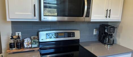 A kitchen with white cabinets, a stainless steel microwave, a black stove, and a coffee maker.
