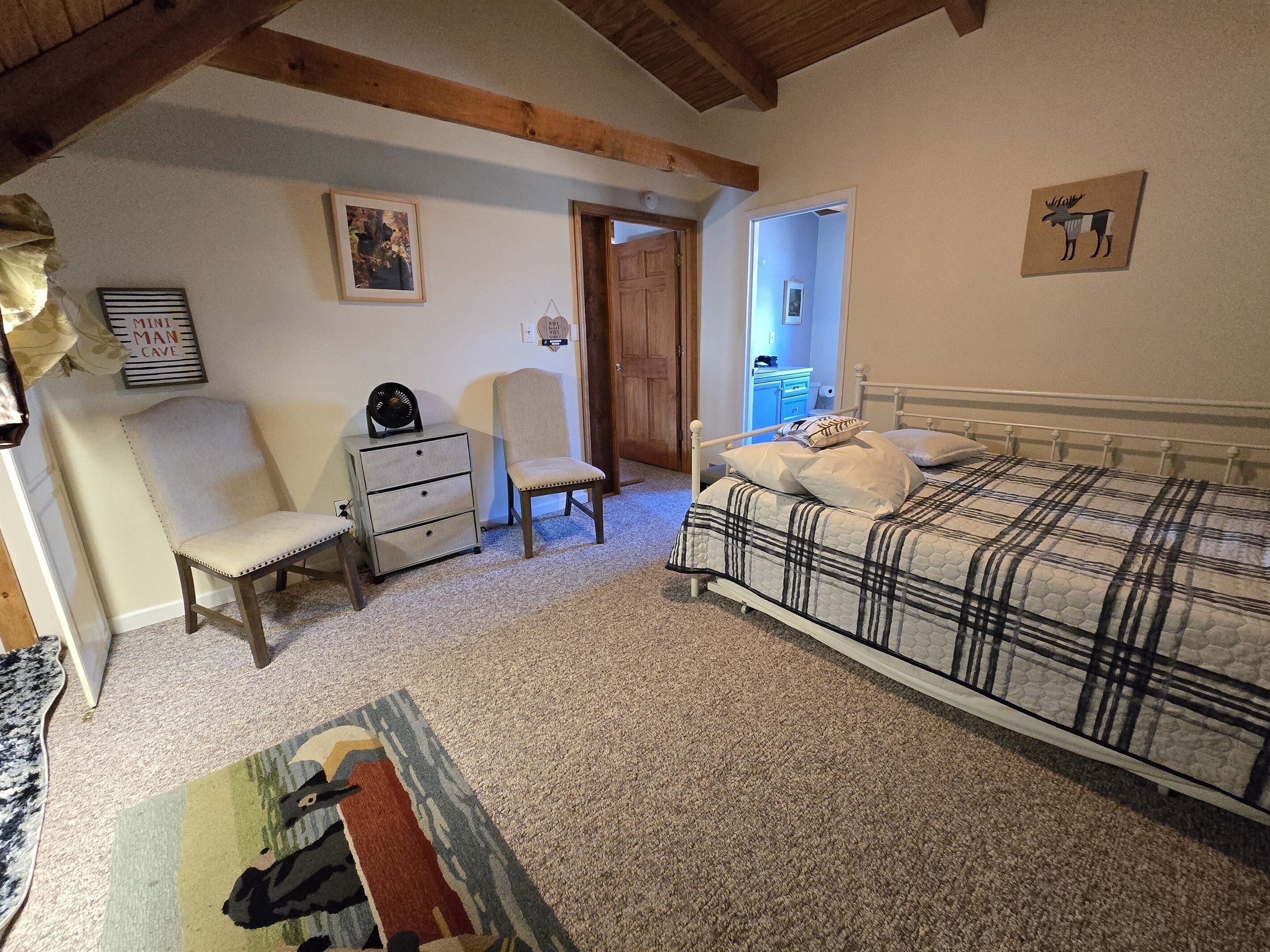 Ein Schlafzimmer mit einem Bett, einem Sessel, einer Kommode und einer Tür zu einem anderen Raum.