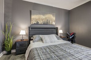 Une chambre à coucher avec un lit, deux tables de chevet, une commode, un grand tableau et une plante en pot.