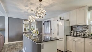 A modern kitchen with a central island, white cabinetry, and a unique chandelier. - Spacious Pool House – 5 Minutes to Elgin Centre (St. Thomas)