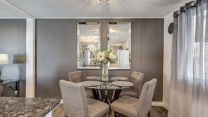 A dining area with a glass table, four upholstered chairs, a vase with flowers, and two wall mirrors. - Spacious Pool House – 5 Minutes to Elgin Centre (St. Thomas)