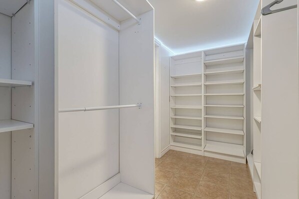 A walk-in closet with open shelving and a hanging rod, tiled floor, and white walls.