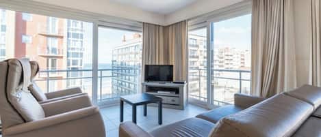 Une chambre d’hôtel moderne dotée d’une grande fenêtre, d’un téléviseur à écran plat, d’un canapé et d’une petite table.