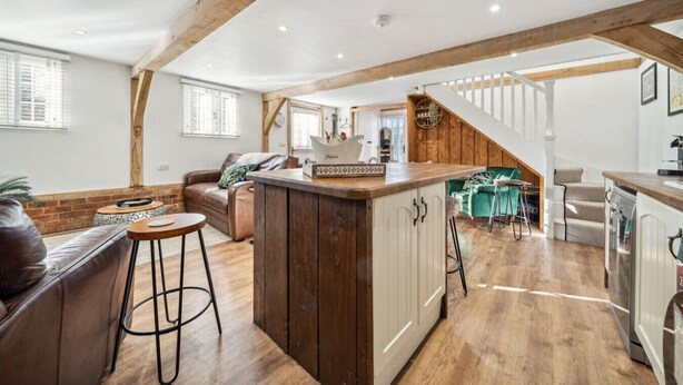 A spacious loft with a kitchen area, wooden beams, and a staircase leading to an upper level. - Peaceful barn stay near Lymington with private garden (Lymington)