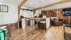 A modern kitchen with a central island, bar stools, a wooden dining table, and a cozy seating area with a leather sofa and a TV. - Peaceful barn stay near Lymington with private garden (Lymington)