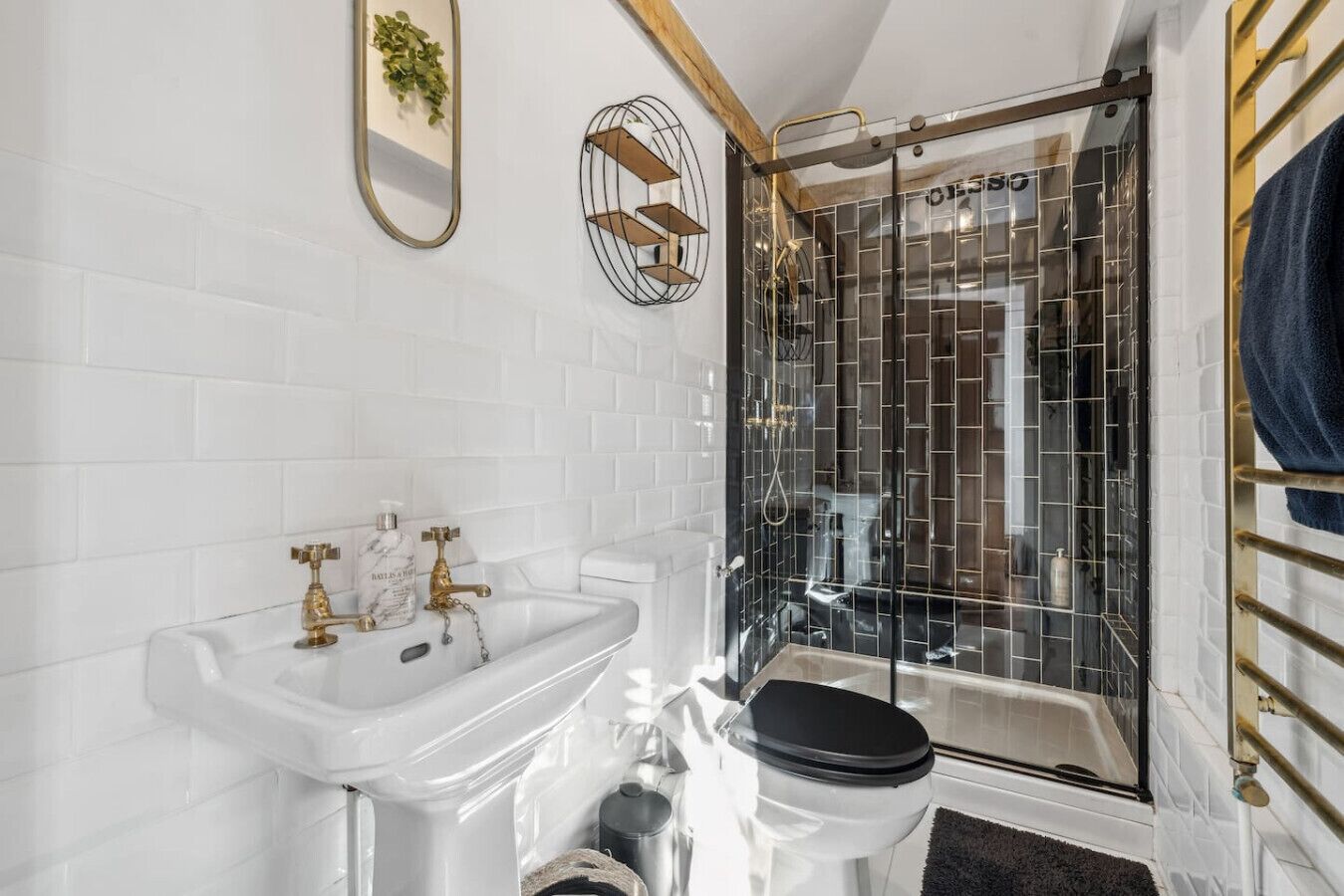 Ein modernes Badezimmer mit einem weißen Waschbecken, goldenen Armaturen, einer schwarzen Toilette und einer Duschkabine aus Glas.