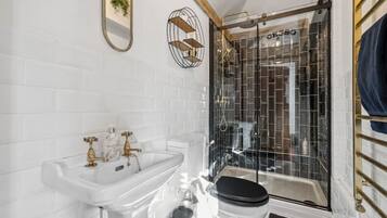 Ein modernes Badezimmer mit einem weißen Waschbecken, goldenen Armaturen, einer schwarzen Toilette und einer Duschkabine aus Glas.