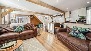 A spacious living area with two leather sofas, a wooden staircase, and a kitchen in the background. - Peaceful barn stay near Lymington with private garden (Lymington)