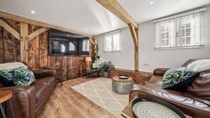 A spacious living room with a wooden ceiling, leather sofas, a coffee table, and a TV mounted on the wall. - Peaceful barn stay near Lymington with private garden (Lymington)