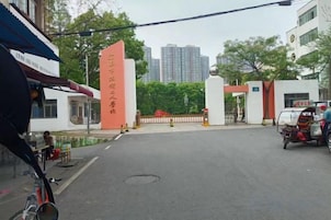 Una entrada con portón y un alto letrero rojo, cielo despejado y un edificio al fondo.