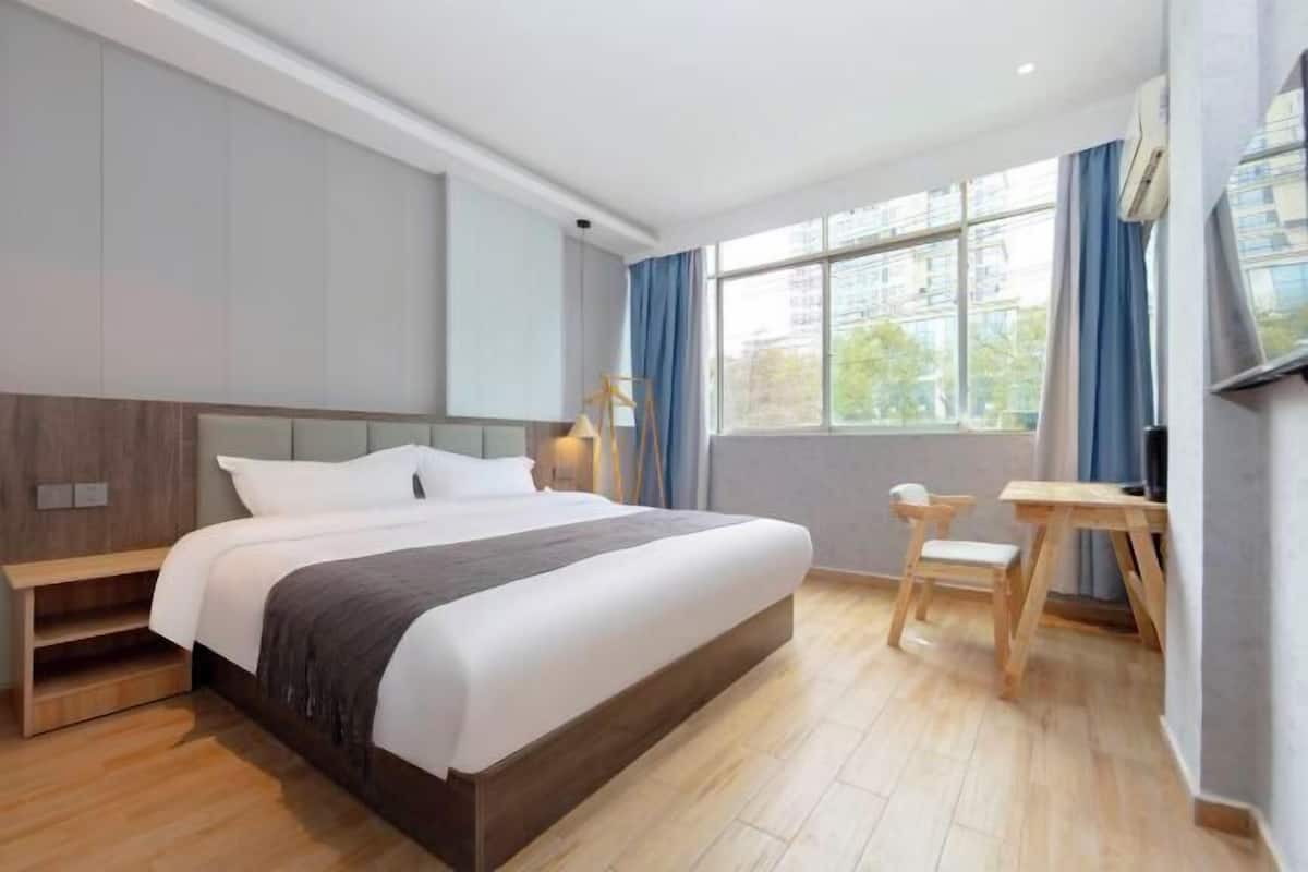 Una habitación de hotel moderna con una cama grande, una mesita de noche de madera, un escritorio y una silla.