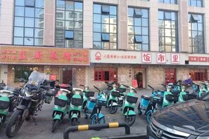 Un edificio con varias tiendas, un estacionamiento con varias scooters y un coche en primer plano.