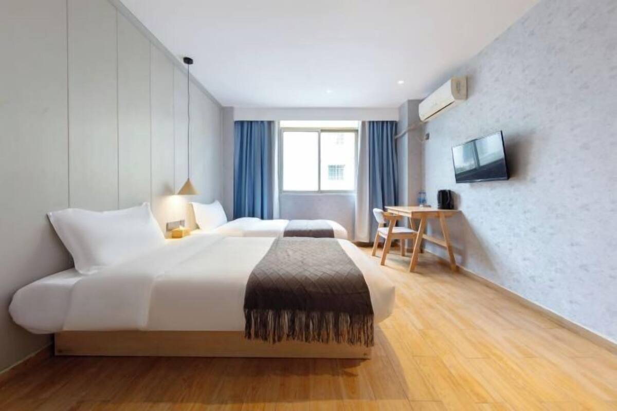Habitación de hotel con dos camas, un escritorio, un televisor y una ventana con cortinas.